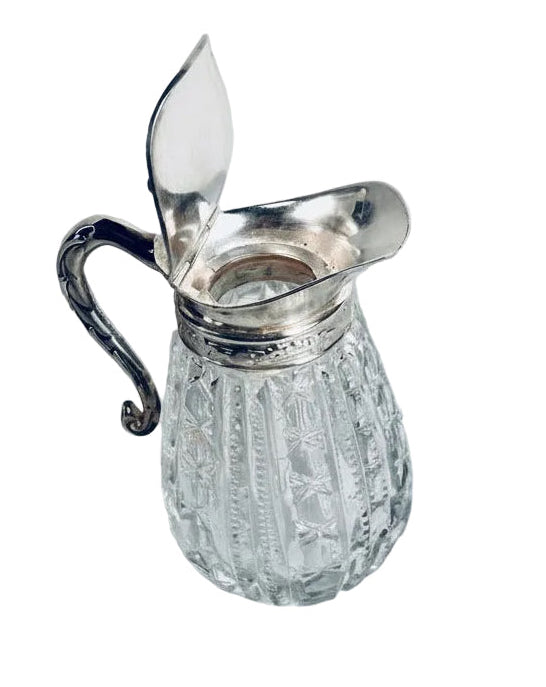 Clear glass pitcher with silver handle on a marble surface
