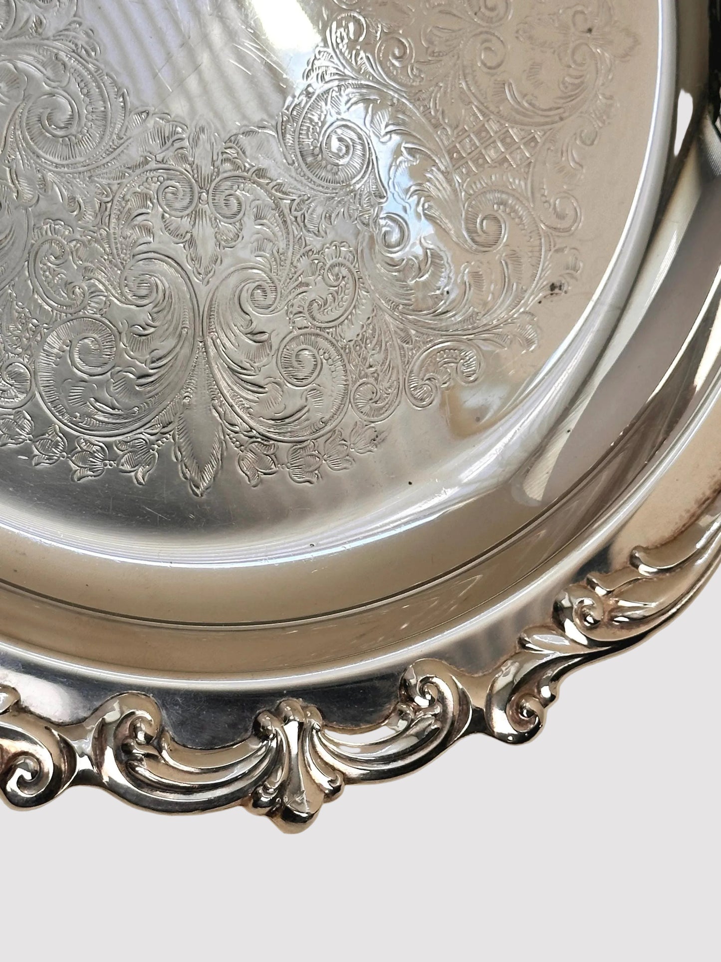 Close-up of an ornate silver platter with detailed engravings on a beige background
