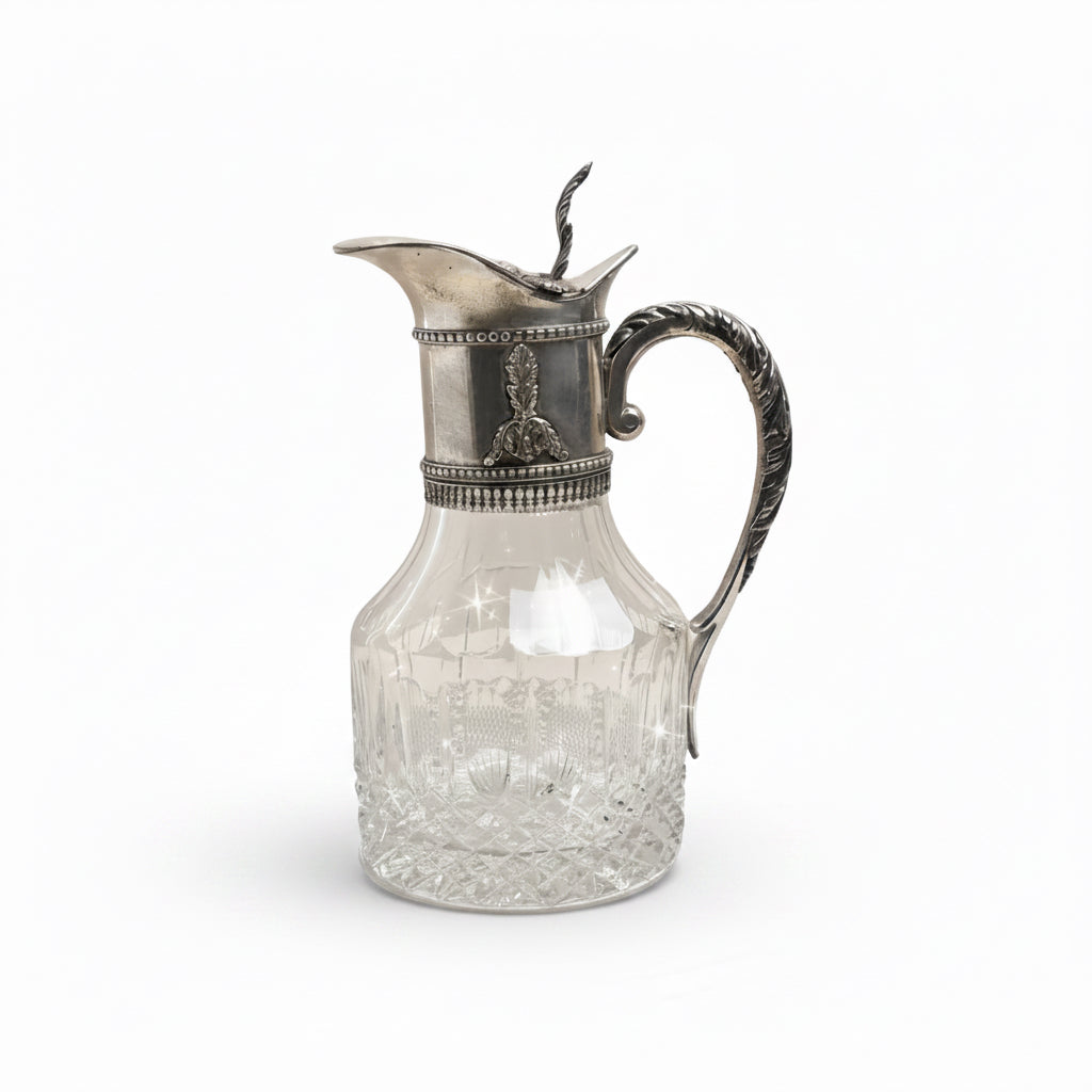 Decorative glass pitcher with silver lid and handle on a plain background