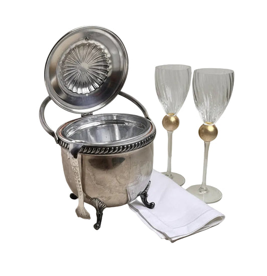 Silver cocktail shaker with two wine glasses on a light surface.