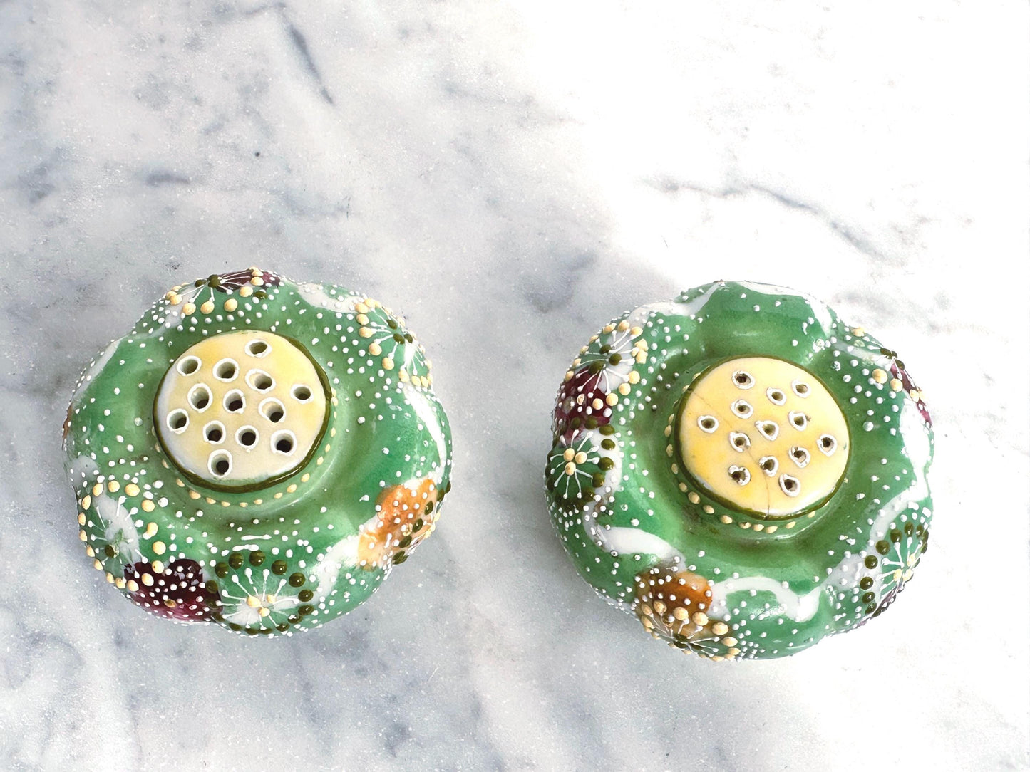 Two decorative salt and pepper shakers with floral patterns on a marble surface.