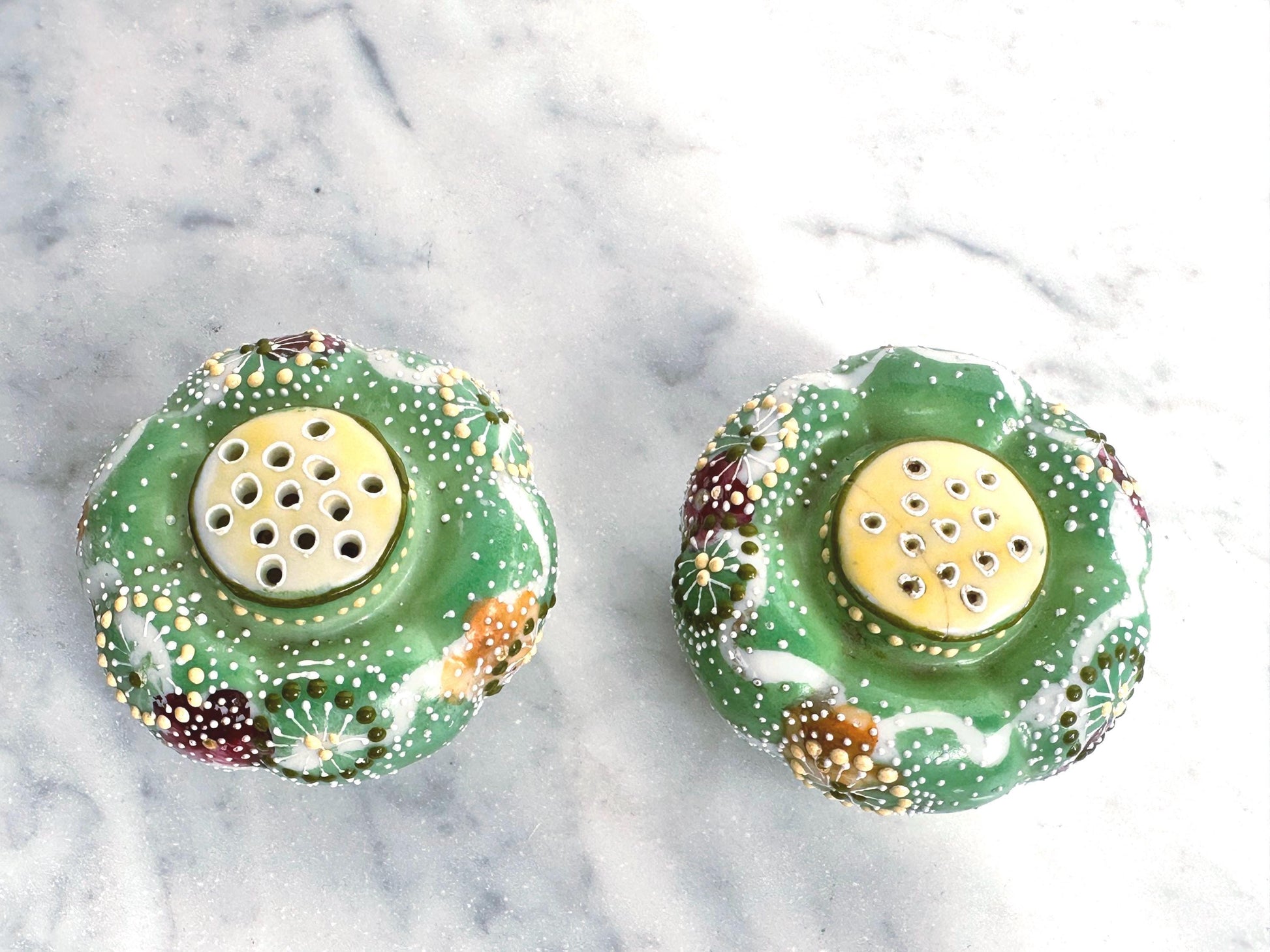 Two decorative salt and pepper shakers with floral patterns on a marble surface.