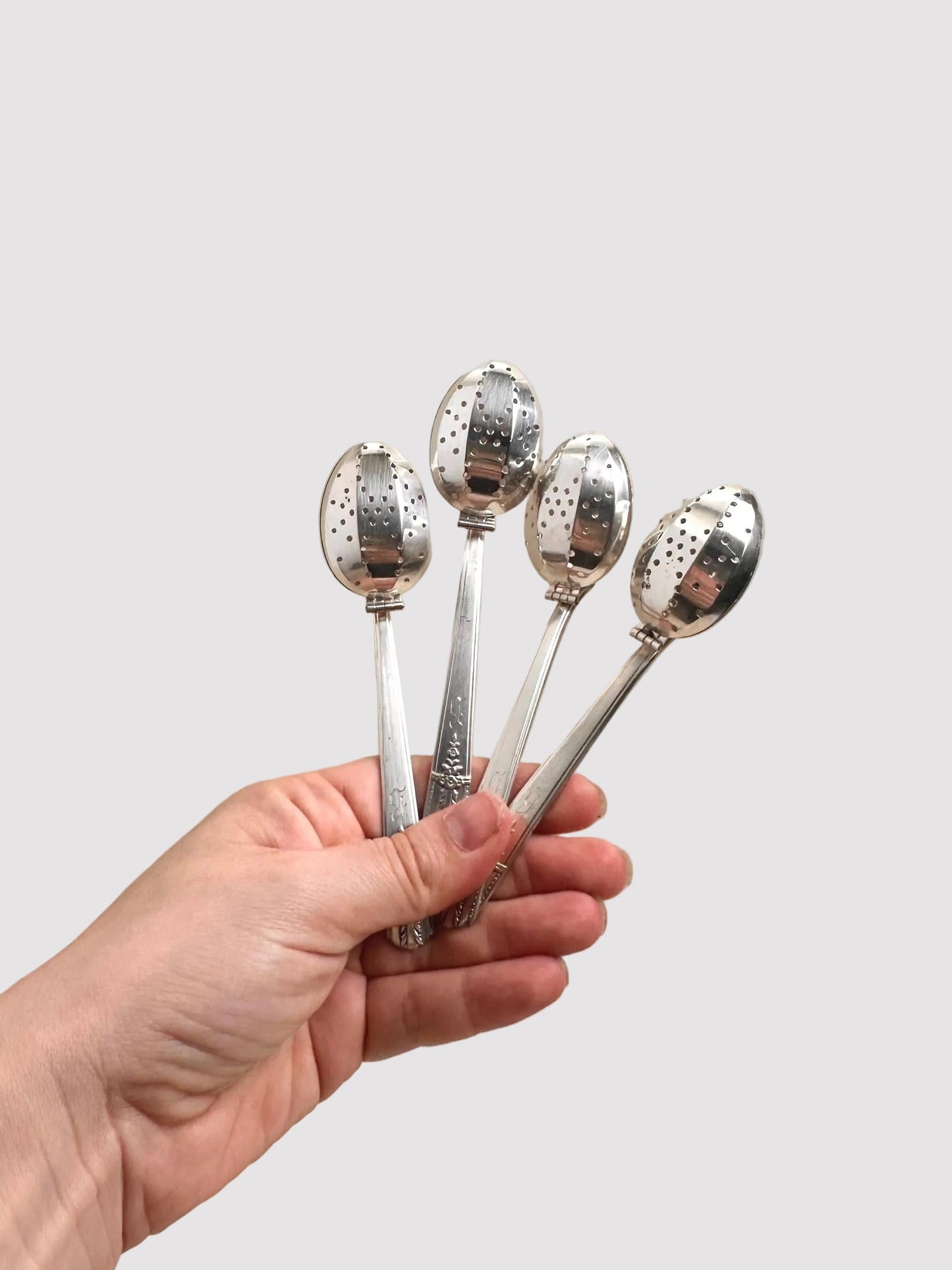 Hand holding four silver spoons with decorative ends against a beige background