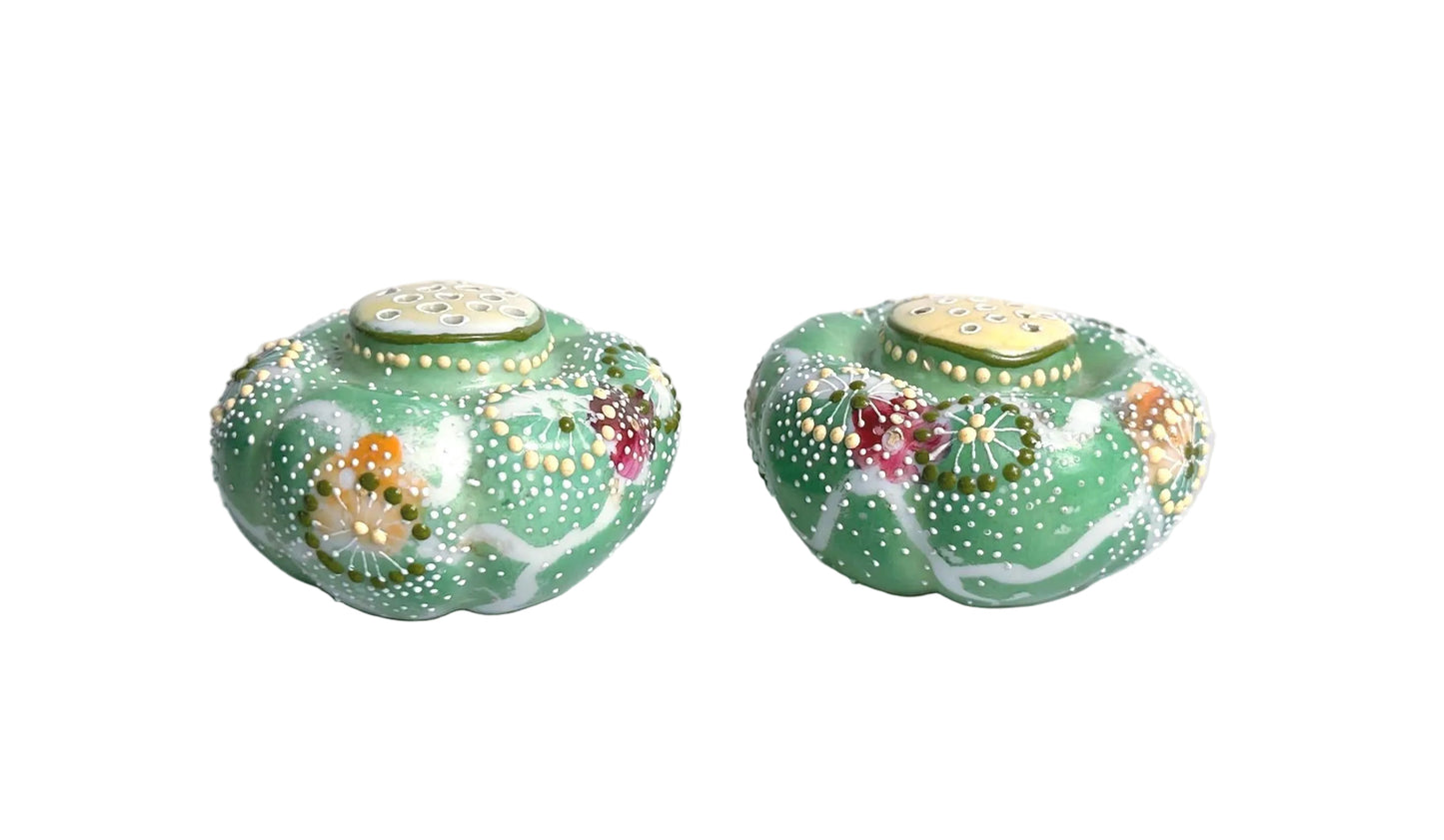 Two decorative green jars with floral patterns on a marble surface