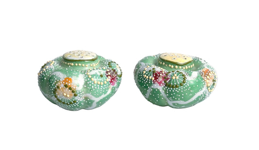 Two decorative green jars with floral patterns on a marble surface