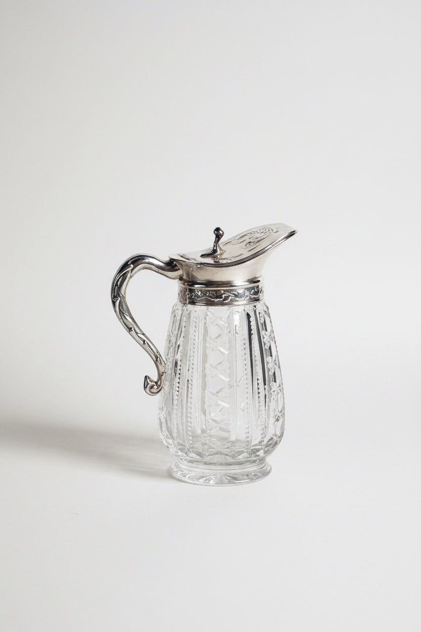Clear glass pitcher with silver lid and handle on a marble surface