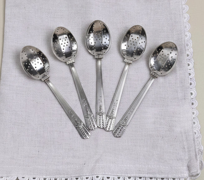Four silver spoons on a white napkin with lace edge against a beige background
