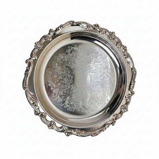 Silver decorative tray with intricate designs on a beige background