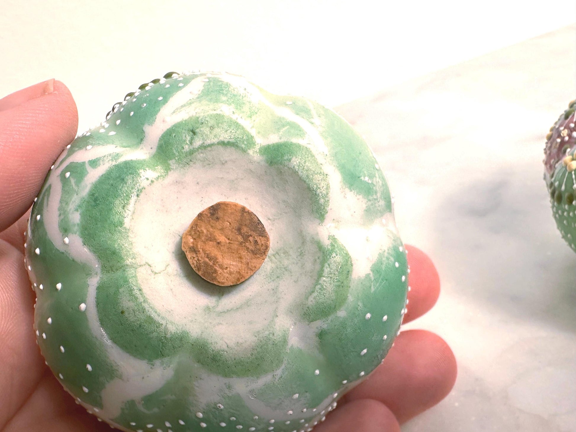 Green marbled donut with a gold center held by a hand against a white background