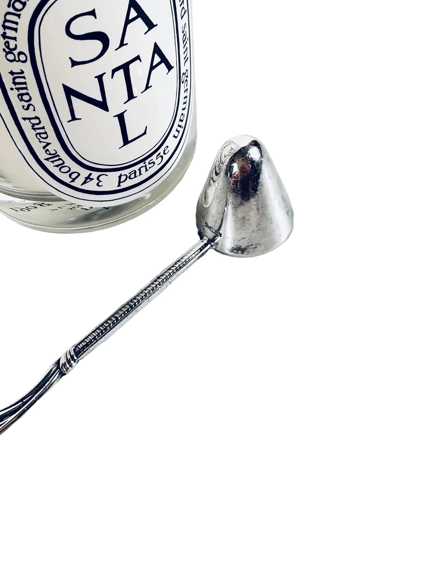 Silver ladle next to a Santal 13 Diptyque perfume bottle on a marble surface