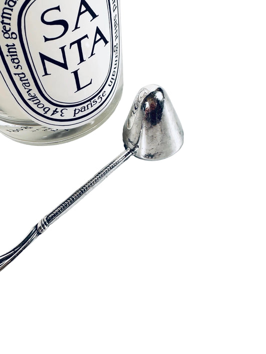 Silver ladle next to a Santal 13 Diptyque perfume bottle on a marble surface