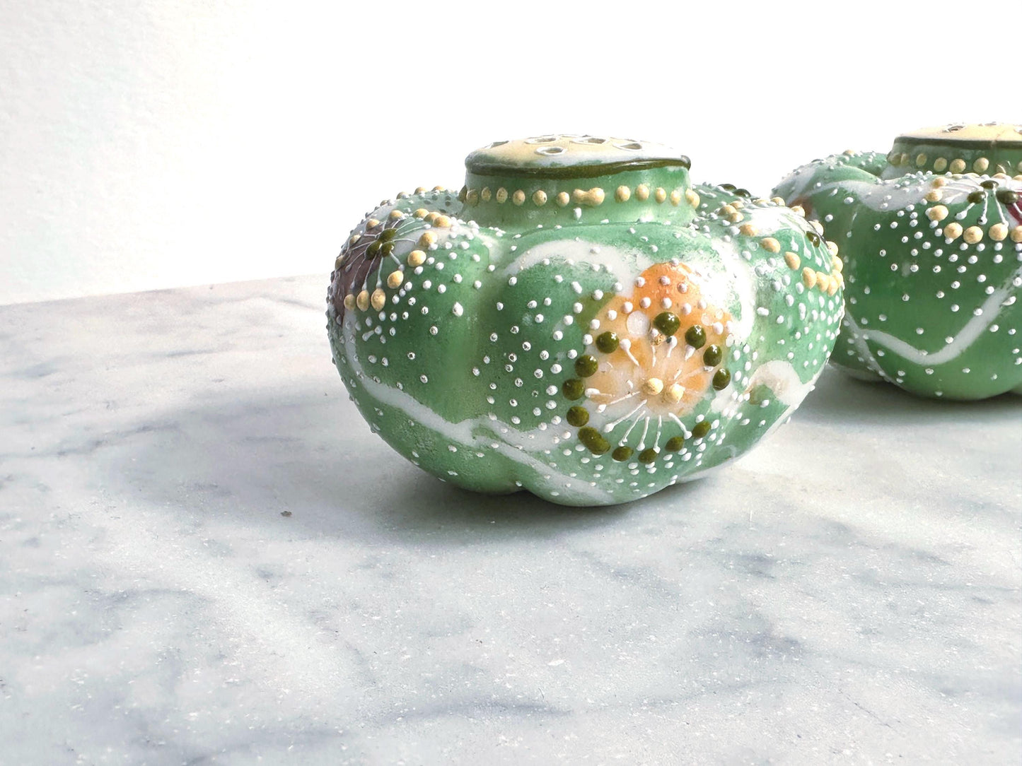 Decorative green ceramic pots with floral patterns on a marble surface