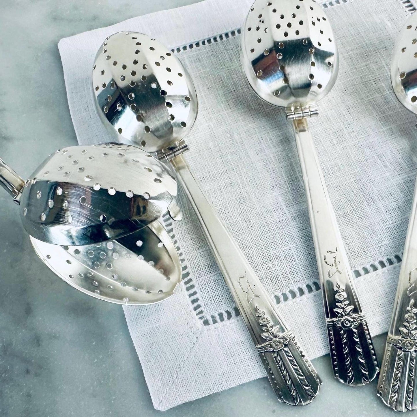 Silver tea infusers on a textured surface