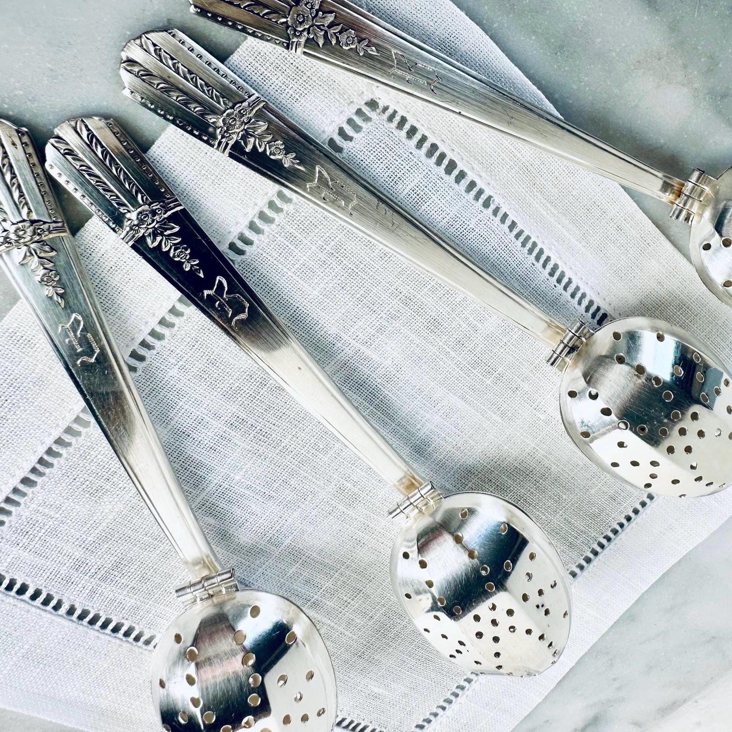 Set of silver spoons with decorative handles on a textured white surface