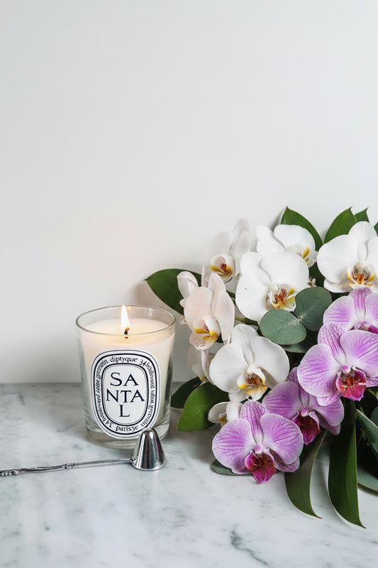 Diptyque Santal candle in a glass jar with a metal wick trimmer on a marble surface.